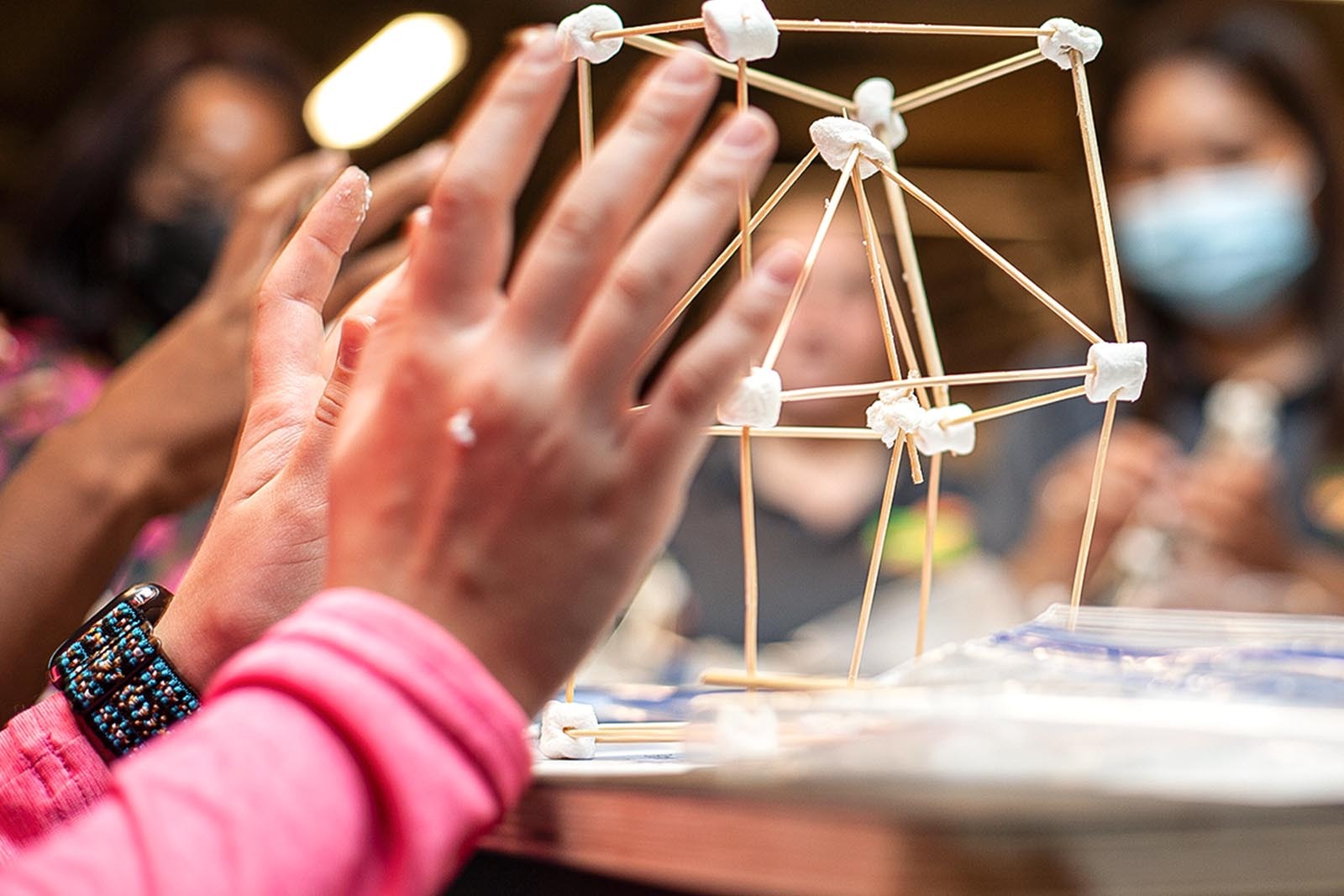 close up photo of a girl's hands working on a marshmallow and toothpick structure. 