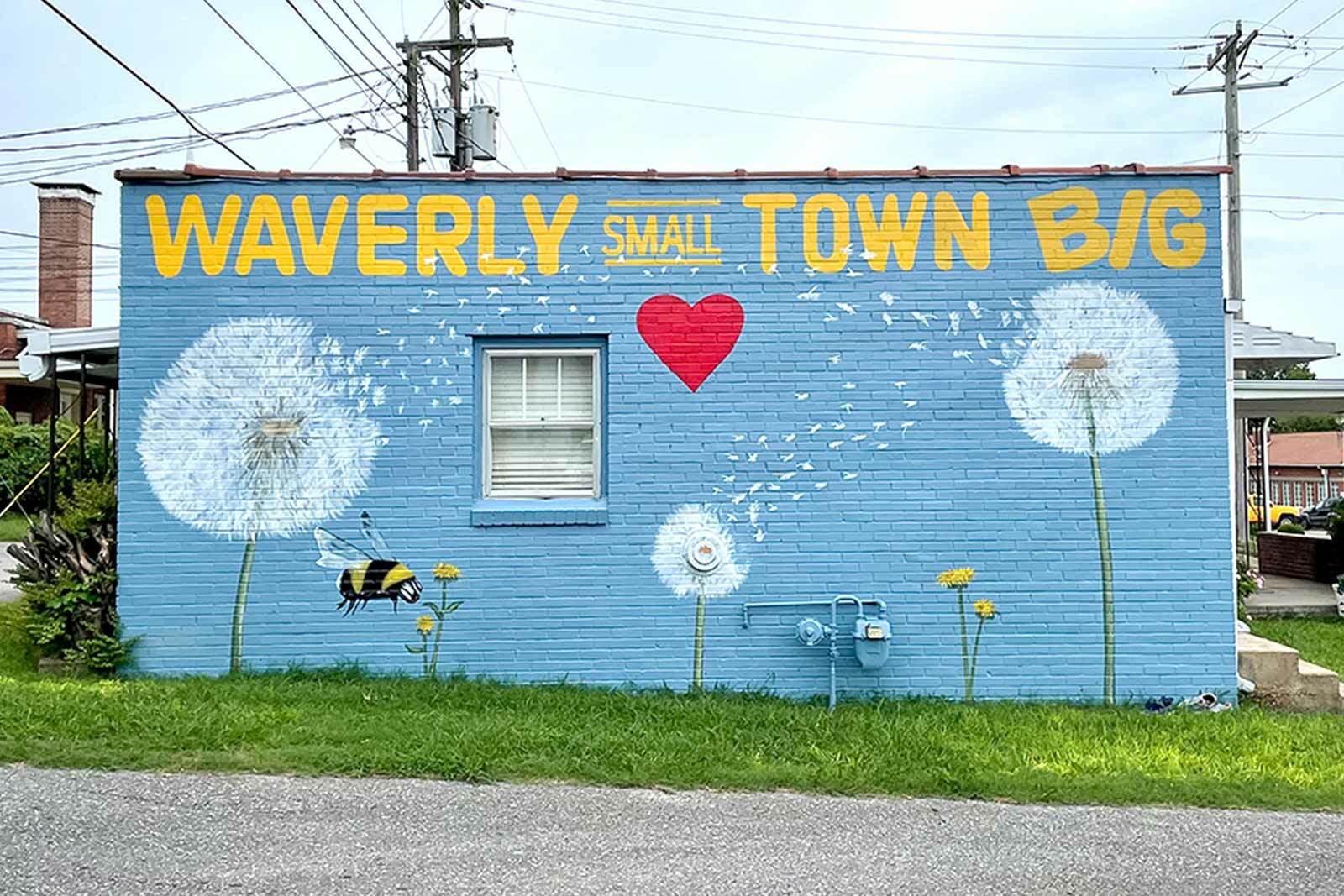 Photo of a mural of dandelions and a bumble bee. Text on the mural says, " Waverly, Small Town, Big Heart."