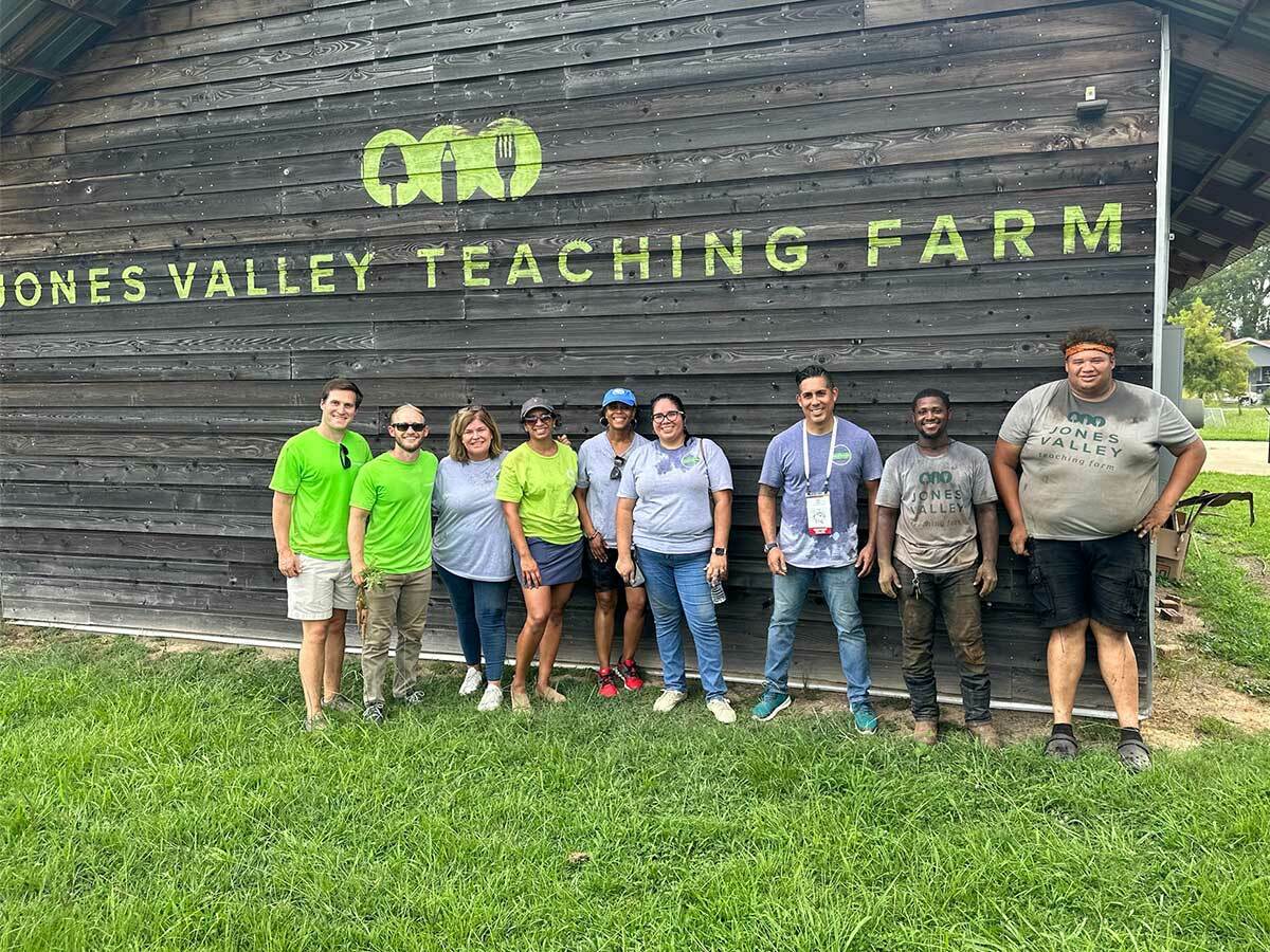 Photo of Regions associate volunteers in front of the Jones Valley Teaching Farm sign