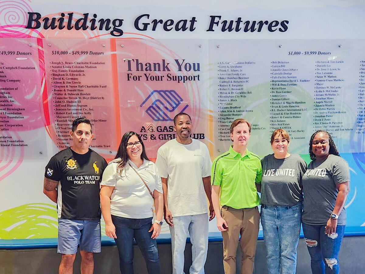 Alt Text: Photo of a Regions volunteer group in front of the “Building Great Futures” display inside A.G. Gaston Boys & Girls Club