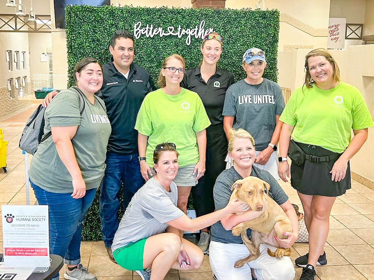 Photo of Regions volunteers with one of the Greater Birmingham Humane Society’s dogs in front of a green grassy-like background with the words “Better Together” appearing in white at the top.