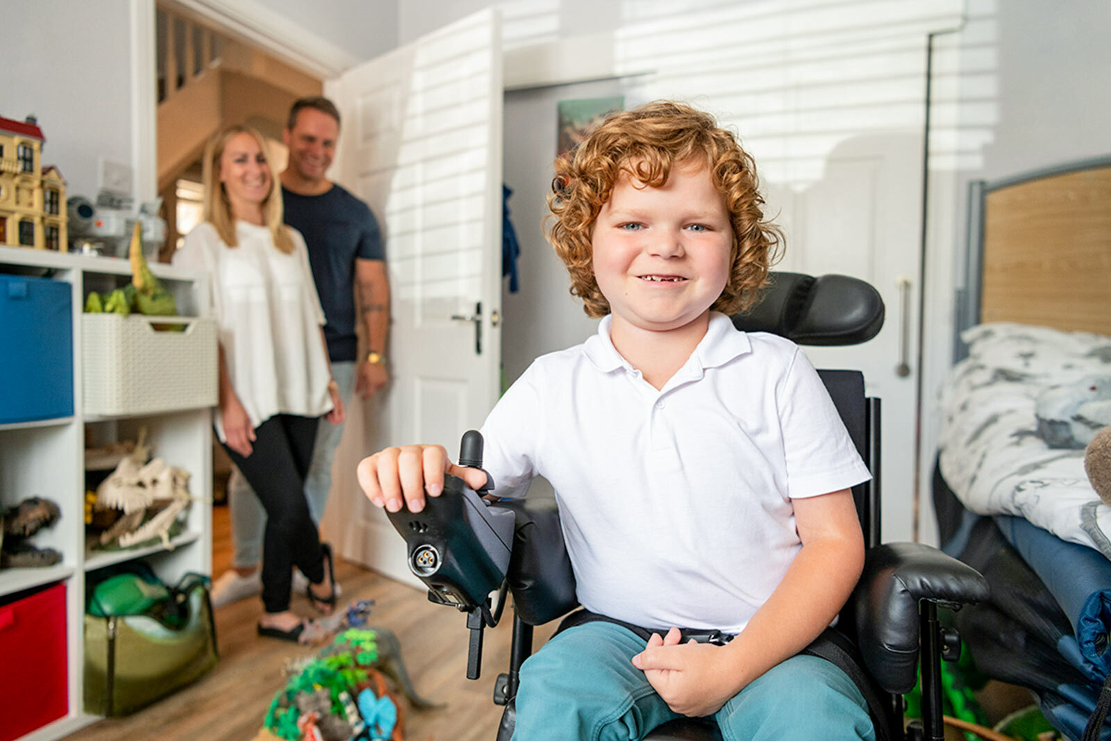 Young boy in his bedroom using wheelchair, mother and father...