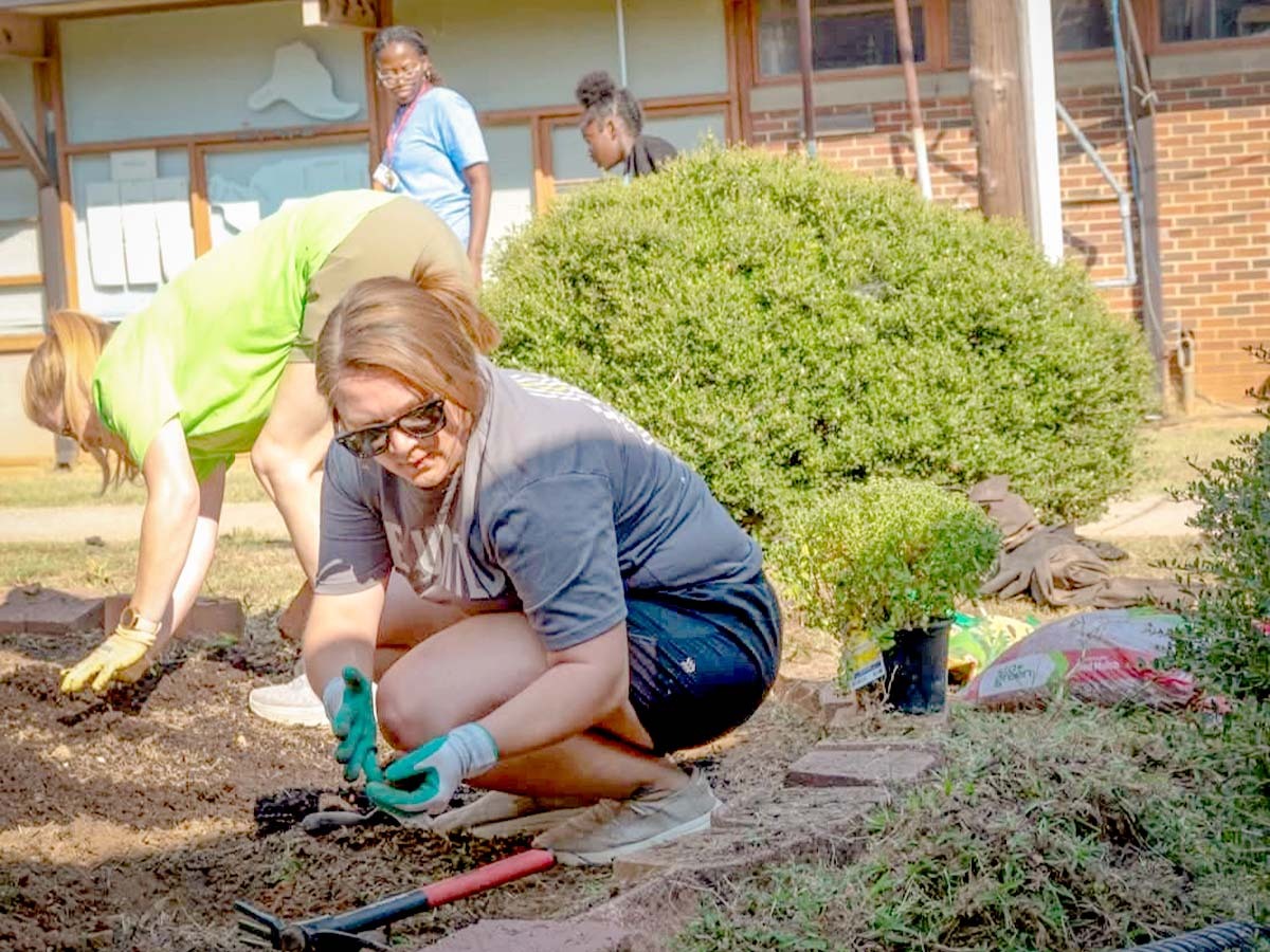 Group of four women working in a garden with one woman crouched down to the ground as the focal point.
