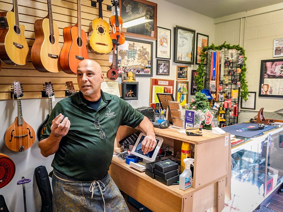 Manuel Delgado in front of a wall of string instruments.