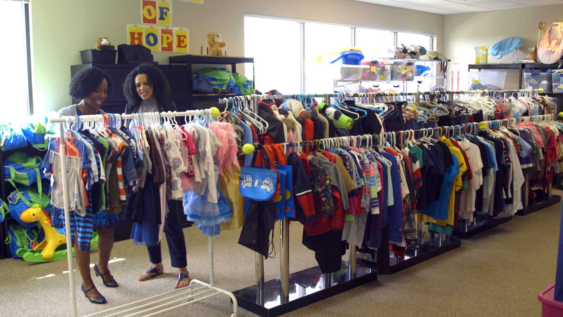 two women looking at children's clothing on racks