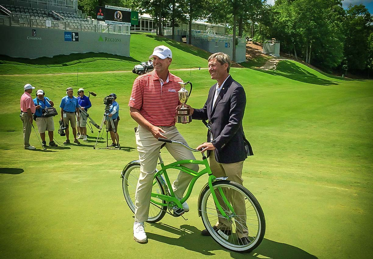 golfer on bike, holding trophy, with bank executive standing